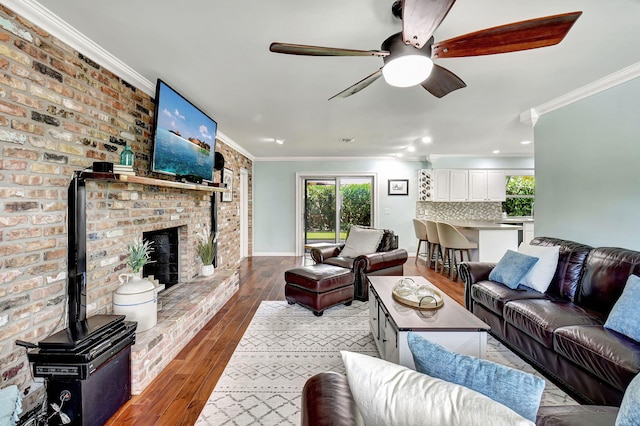 living area with baseboards, wood-type flooring, ceiling fan, ornamental molding, and a fireplace