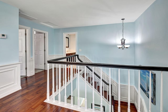 hallway featuring visible vents, a wainscoted wall, wood finished floors, an upstairs landing, and a decorative wall