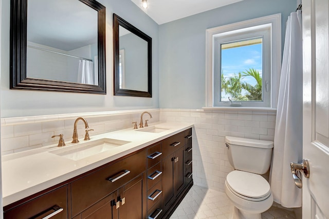 bathroom featuring toilet, double vanity, a sink, and tile walls