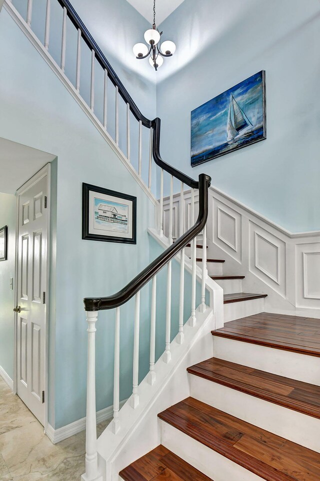 stairs featuring a wainscoted wall, a decorative wall, a towering ceiling, and an inviting chandelier