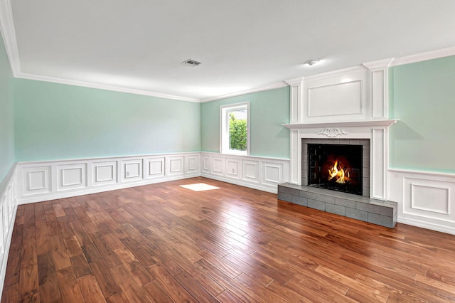 unfurnished living room featuring a decorative wall, a fireplace, wood finished floors, visible vents, and crown molding