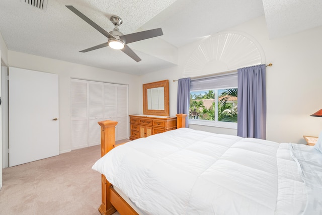 bedroom with a textured ceiling, a closet, ceiling fan, and light colored carpet