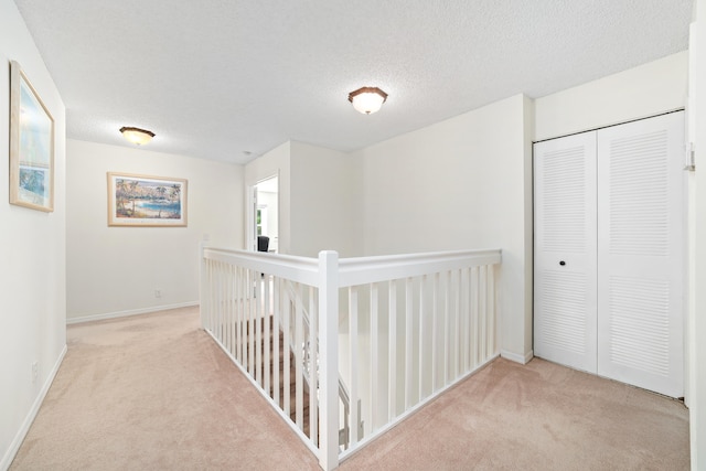 hallway with a textured ceiling and light carpet