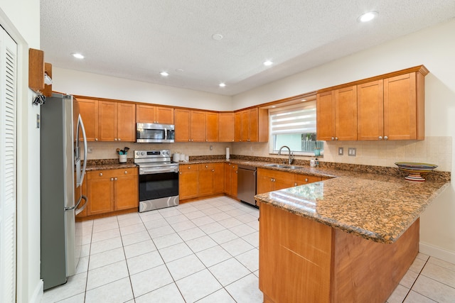 kitchen featuring kitchen peninsula, stainless steel appliances, a textured ceiling, and dark stone countertops