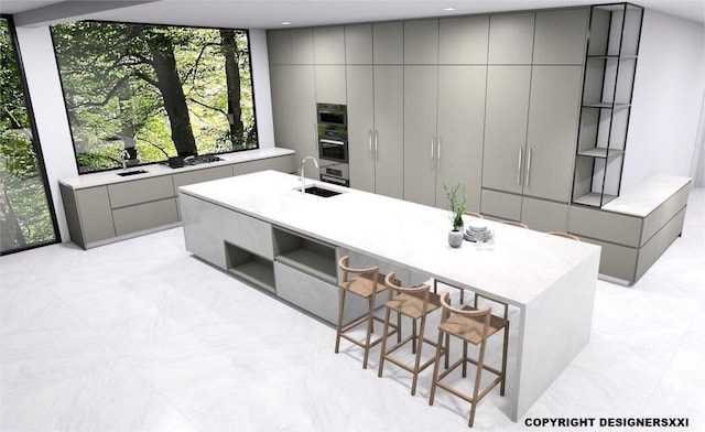 kitchen featuring gray cabinetry, sink, stainless steel oven, a breakfast bar area, and a kitchen island with sink