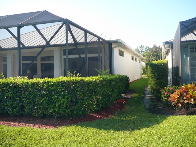 view of property exterior featuring a lanai, a yard, and a standing seam roof