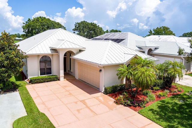 view of front facade featuring a garage, concrete driveway, metal roof, a standing seam roof, and stucco siding