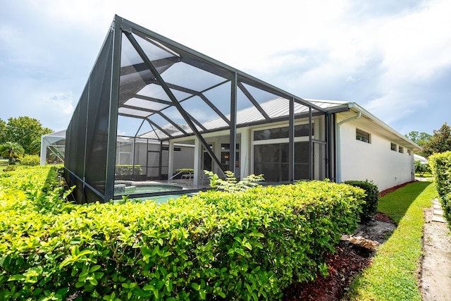 back of house featuring glass enclosure, an outdoor pool, and stucco siding