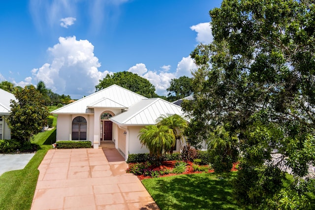 view of front of property with a standing seam roof, metal roof, a front lawn, and stucco siding