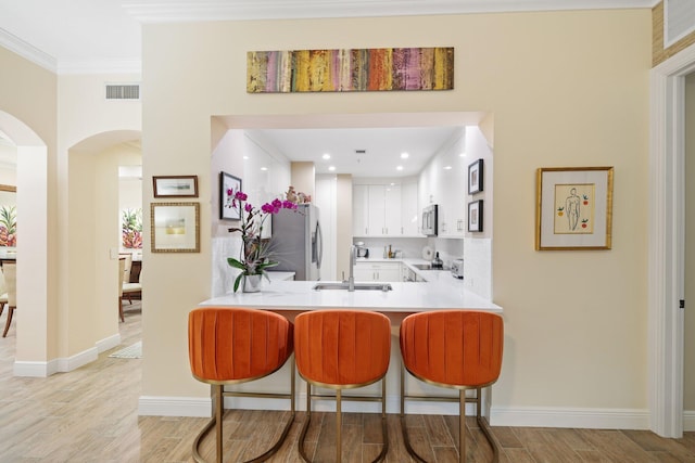 kitchen featuring a kitchen breakfast bar, sink, light hardwood / wood-style floors, white cabinetry, and kitchen peninsula