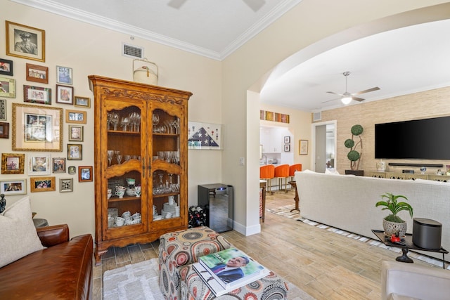 living room with light wood-type flooring, ornamental molding, and ceiling fan