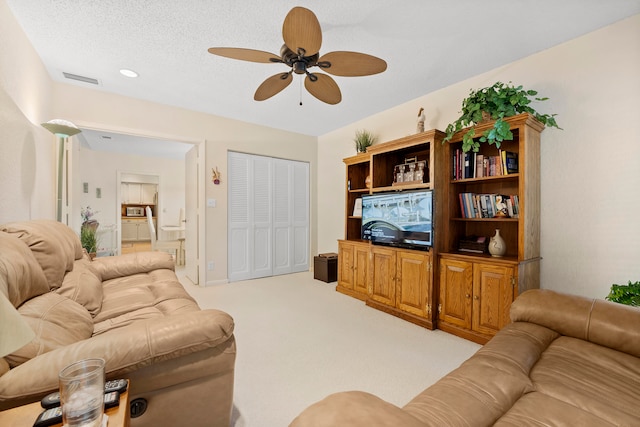 living room with ceiling fan, a textured ceiling, and light carpet