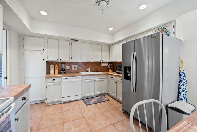 kitchen with decorative backsplash, sink, light tile patterned floors, white dishwasher, and stainless steel fridge