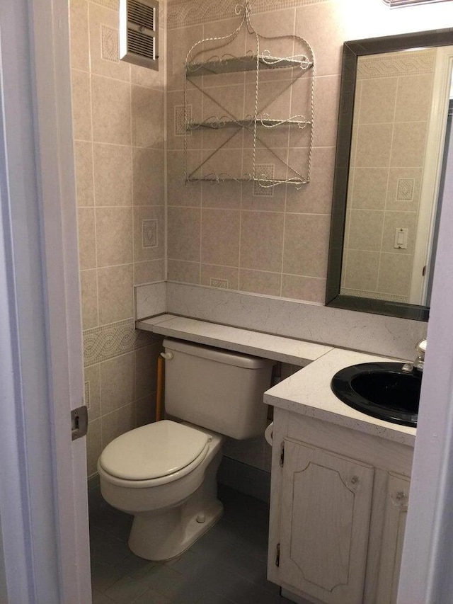 bathroom featuring toilet, vanity, and tile walls