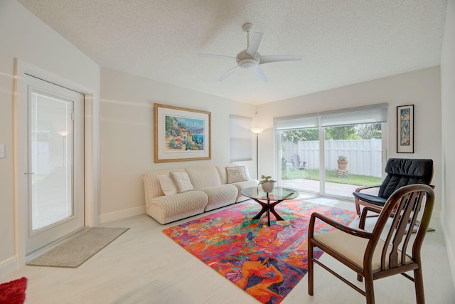 living room with a textured ceiling, ceiling fan, and light wood-type flooring