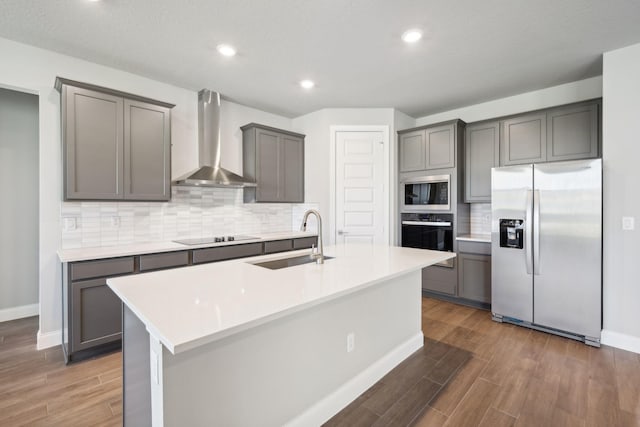 kitchen with dark wood-type flooring, wall chimney exhaust hood, black appliances, sink, and an island with sink