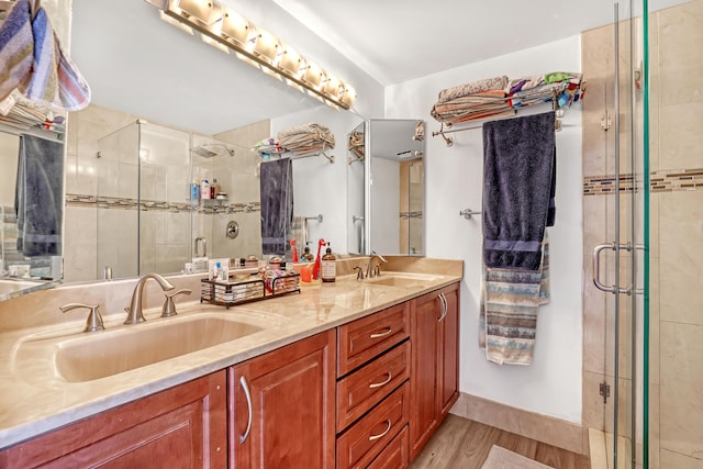 full bathroom with double vanity, wood finished floors, a sink, and a shower stall