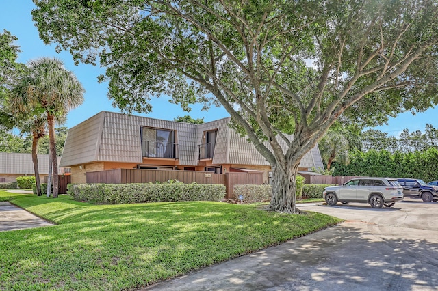 view of front of home with mansard roof, a front lawn, fence, and brick siding