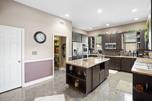 kitchen featuring decorative backsplash, an island with sink, appliances with stainless steel finishes, light tile patterned floors, and sink