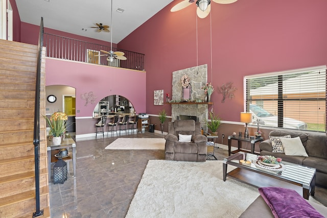 tiled living room with ceiling fan, high vaulted ceiling, and a stone fireplace