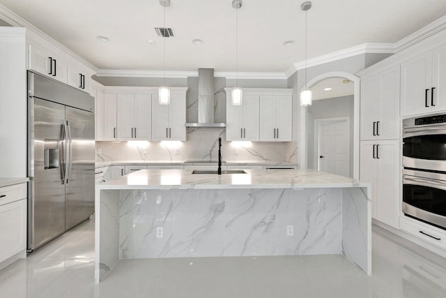 kitchen featuring a center island with sink, decorative light fixtures, wall chimney range hood, and appliances with stainless steel finishes