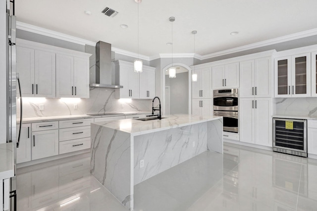 kitchen featuring light stone countertops, hanging light fixtures, beverage cooler, wall chimney range hood, and a kitchen island with sink