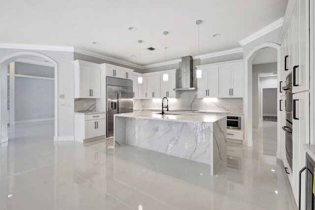 kitchen featuring decorative backsplash, appliances with stainless steel finishes, wall chimney exhaust hood, pendant lighting, and an island with sink