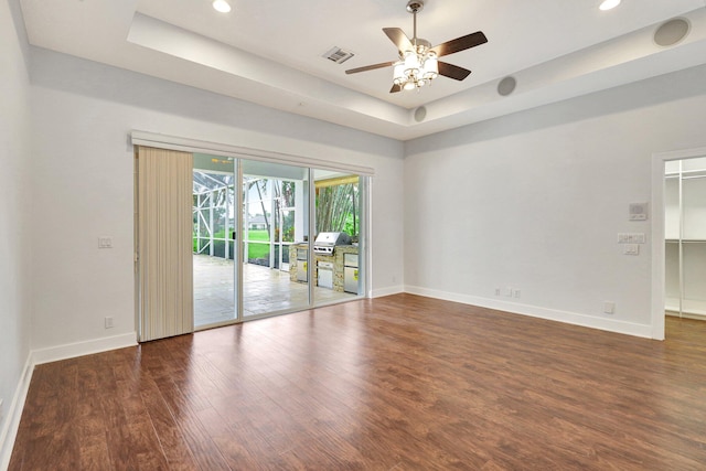 unfurnished room with a tray ceiling, ceiling fan, and dark wood-type flooring