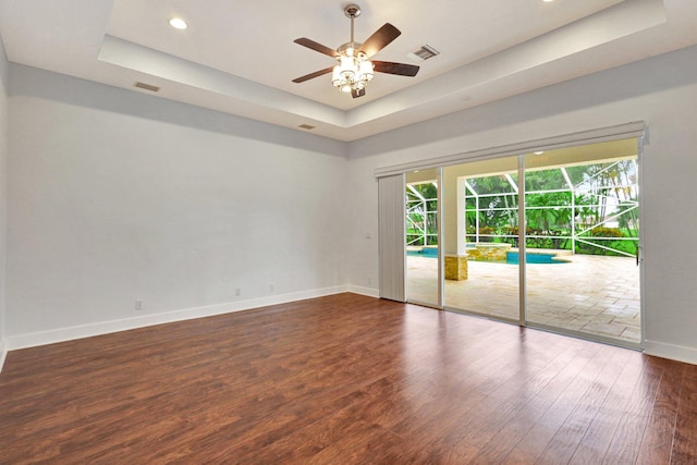 spare room featuring a raised ceiling, ceiling fan, and dark hardwood / wood-style flooring