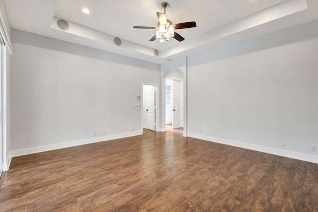 empty room with a tray ceiling, dark hardwood / wood-style floors, and ceiling fan