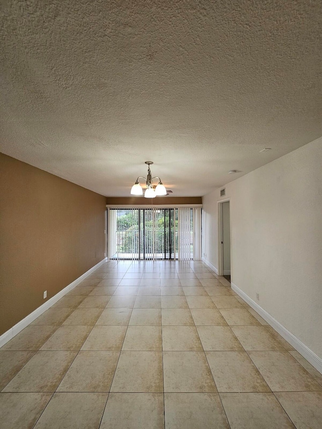 empty room with a textured ceiling, an inviting chandelier, and light tile patterned flooring