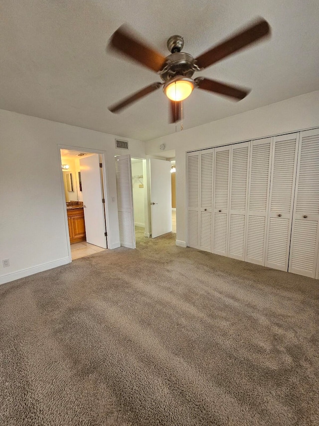 unfurnished bedroom featuring ceiling fan, light carpet, ensuite bathroom, and a closet