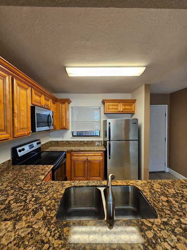 kitchen with sink, stainless steel appliances, a textured ceiling, and dark stone countertops