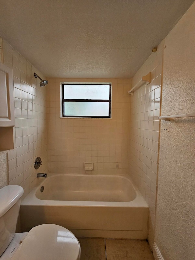 bathroom featuring tile patterned flooring, a textured ceiling, tiled shower / bath combo, and toilet