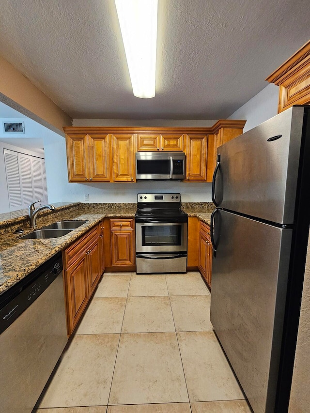 kitchen featuring appliances with stainless steel finishes, light tile patterned floors, sink, dark stone countertops, and a textured ceiling