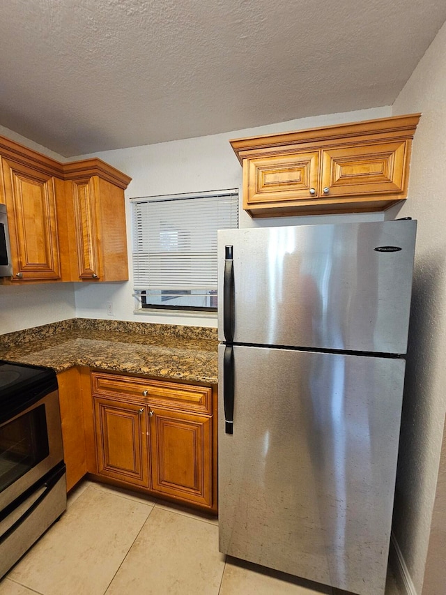 kitchen with appliances with stainless steel finishes, a textured ceiling, light tile patterned floors, and dark stone counters