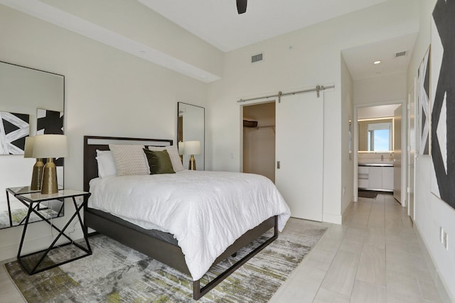 tiled bedroom with ceiling fan, a spacious closet, a barn door, a closet, and ensuite bath