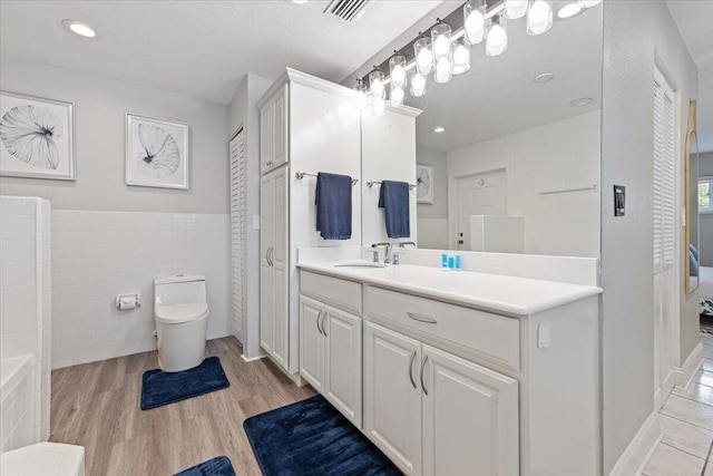 bathroom with hardwood / wood-style flooring, toilet, tile walls, vanity, and a textured ceiling