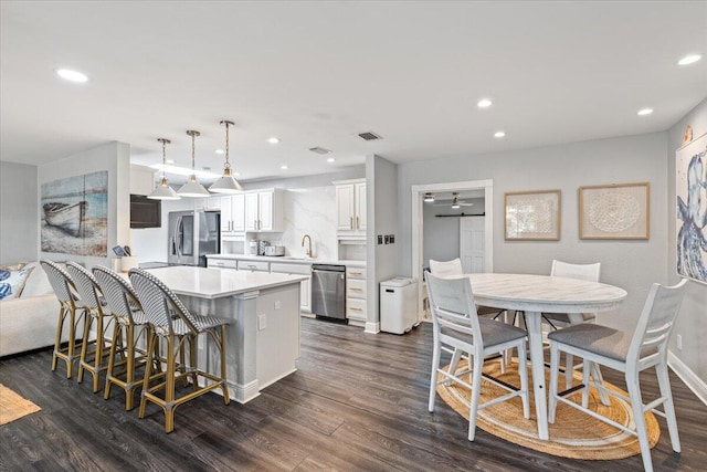 kitchen featuring dark hardwood / wood-style floors, decorative light fixtures, a center island, stainless steel appliances, and white cabinets