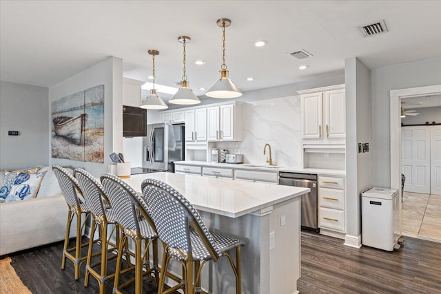 kitchen with decorative light fixtures, appliances with stainless steel finishes, dark hardwood / wood-style flooring, white cabinetry, and a breakfast bar area