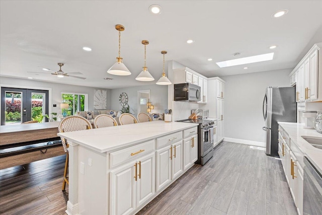 kitchen featuring white cabinetry, a skylight, stainless steel appliances, decorative light fixtures, and a breakfast bar area