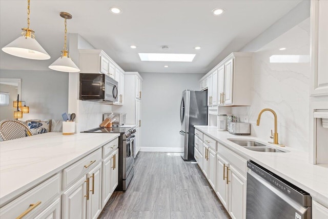 kitchen featuring light stone countertops, appliances with stainless steel finishes, sink, white cabinetry, and a skylight