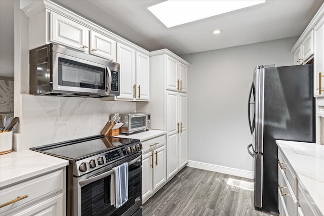 kitchen featuring hardwood / wood-style floors, a skylight, light stone counters, appliances with stainless steel finishes, and white cabinets