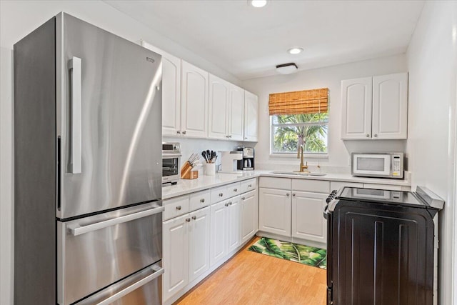 kitchen with light hardwood / wood-style floors, white cabinetry, sink, stainless steel fridge, and stove