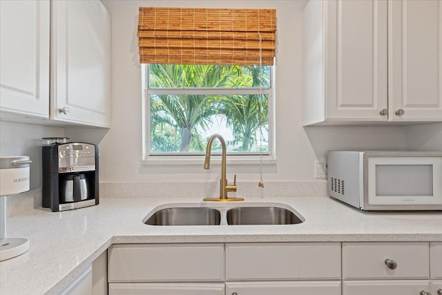 kitchen with light stone counters, sink, and white cabinets