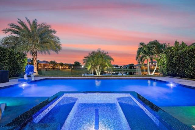 pool at dusk with a water view and an in ground hot tub