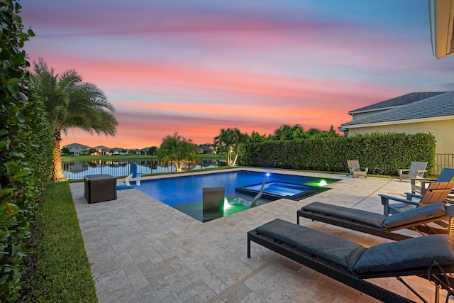 pool at dusk with an in ground hot tub, a water view, and a patio area