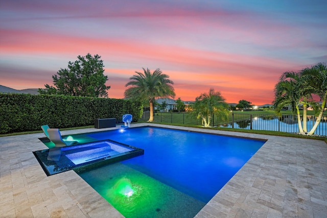 pool at dusk featuring a patio area, a water view, and an in ground hot tub