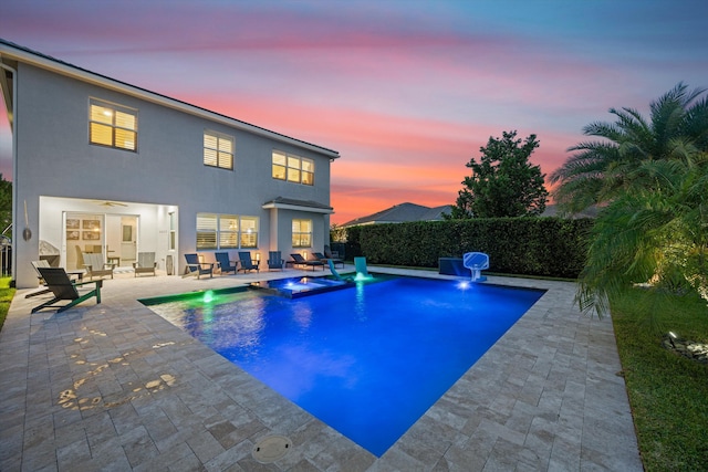 pool at dusk with a patio area and an in ground hot tub