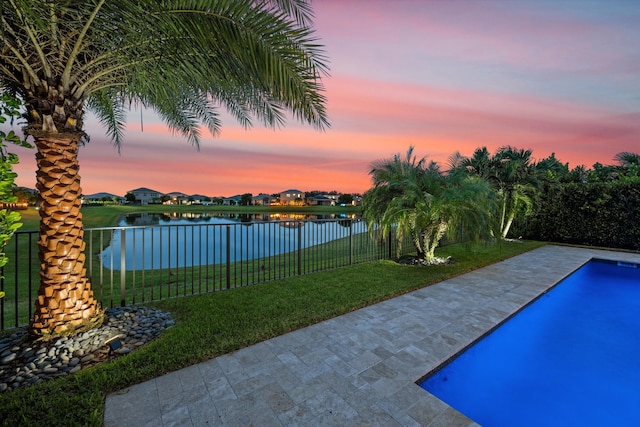 pool at dusk featuring a yard, a water view, and a patio area